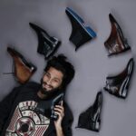 A stylish man lies against a gray background surrounded by leather shoes, showcasing fashion and elegance.